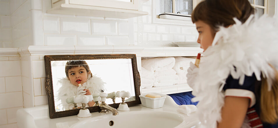 Little girl wearing boa, putting on red lipstick in a mirror