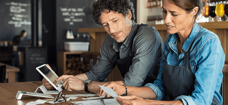 Man and woman sitting at table going through bills at their business.