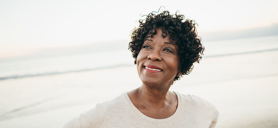 African American woman standing on the beach looking in the distance smiling