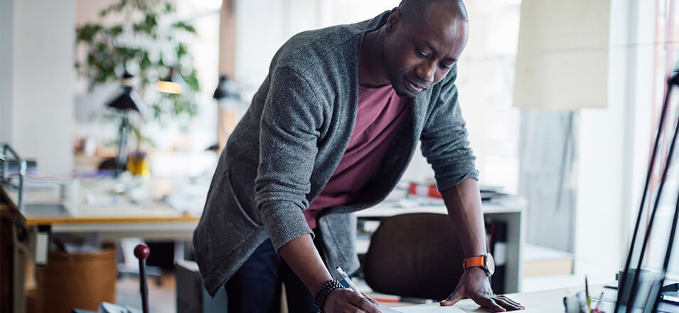 Man standing at desk in office working on drafting papers.