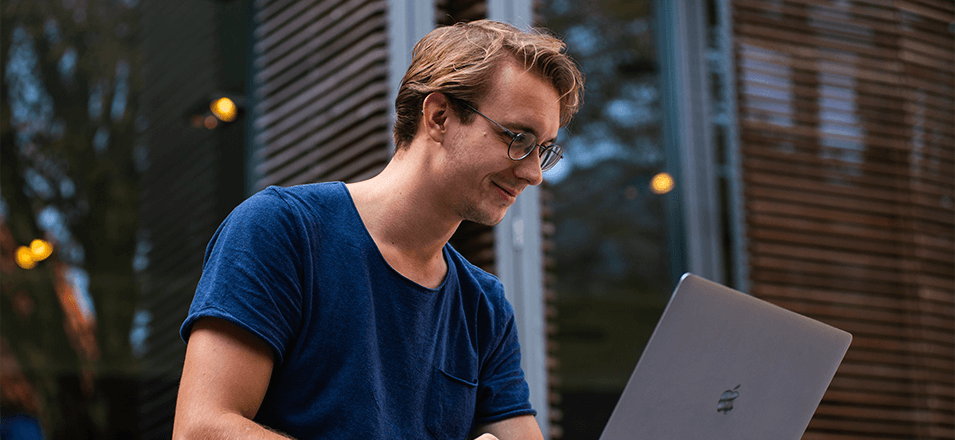 young man sitting outside with laptop on his lap 